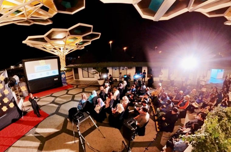 Bezoekers kijken naar een film buiten in een tuin onder de avondhemel, romantische zomeravondsfeer.